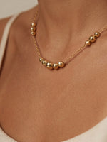 Gold necklace with round beads on a person's neck against a neutral background