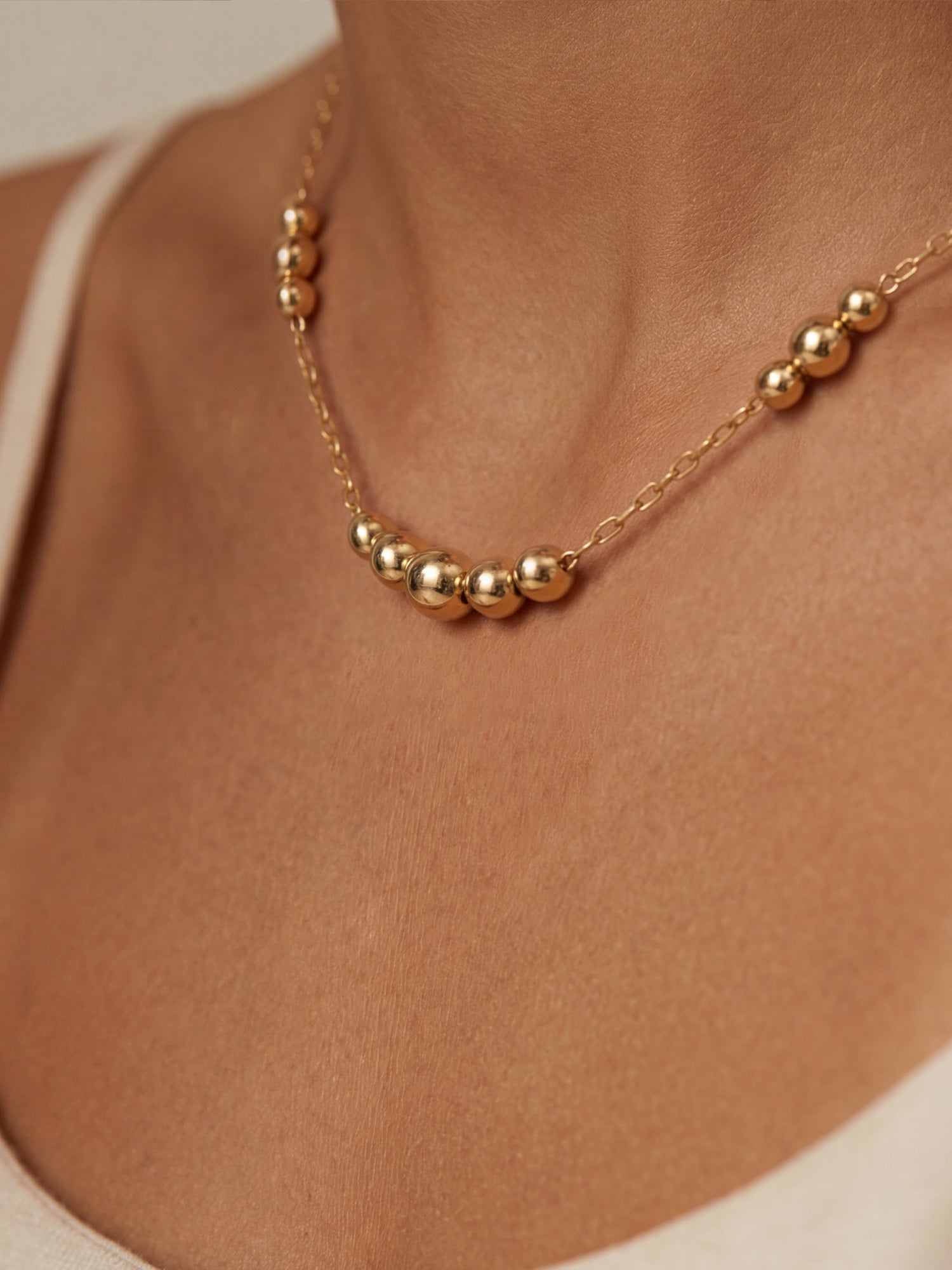 Gold necklace with round beads on a person's neck against a neutral background