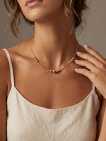 Close-up of a person wearing a delicate gold necklace with a neutral background