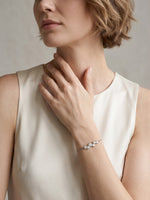 A woman in a white sleeveless top with her hand near her shoulder, elegantly modeling the silver cubic zirconia cluster bracelet on her wrist.
