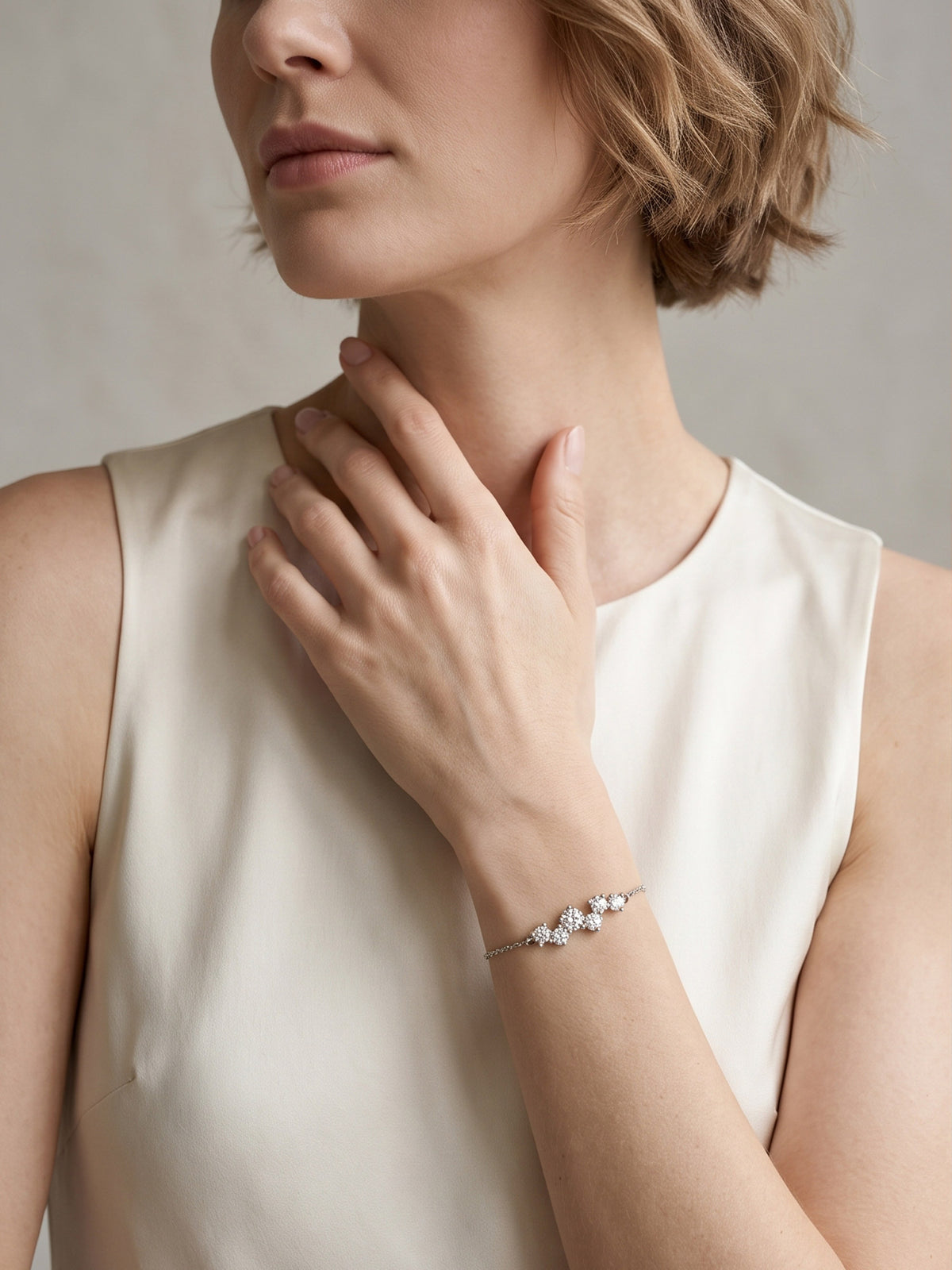 A woman in a white sleeveless top with her hand near her shoulder, elegantly modeling the silver cubic zirconia cluster bracelet on her wrist.